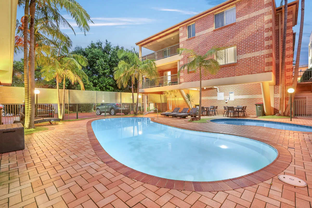 Twilight view of the solar-heated pool, BBQ area kids splash pool at Terralong Terrace Apartments Kiama, with loungers and tropical landscaping